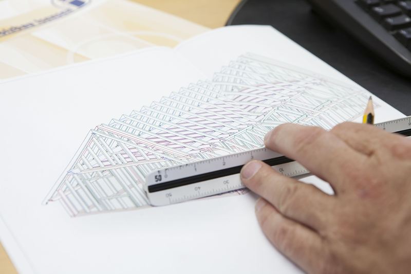 Hand mit Maßstab und Bleistift auf einer Bauzeichnung